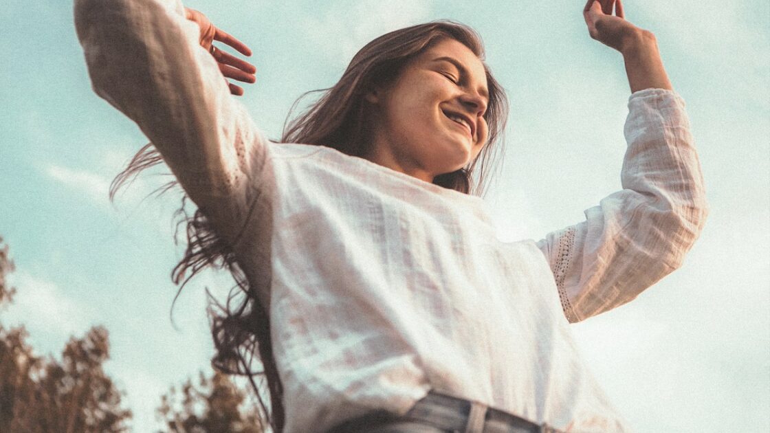 青空に向かって笑顔で両手を広げる女性